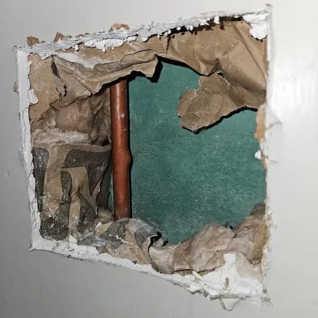 Opened drywall exposes a copper pipe inside a wall.