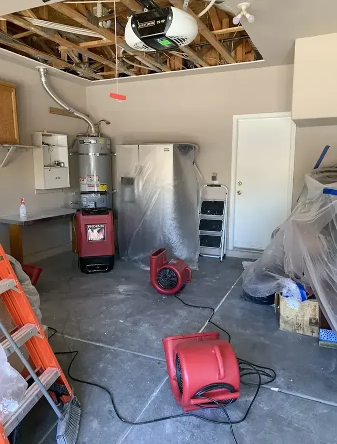 Drying equipment stands in a garage beneath an opened ceiling.