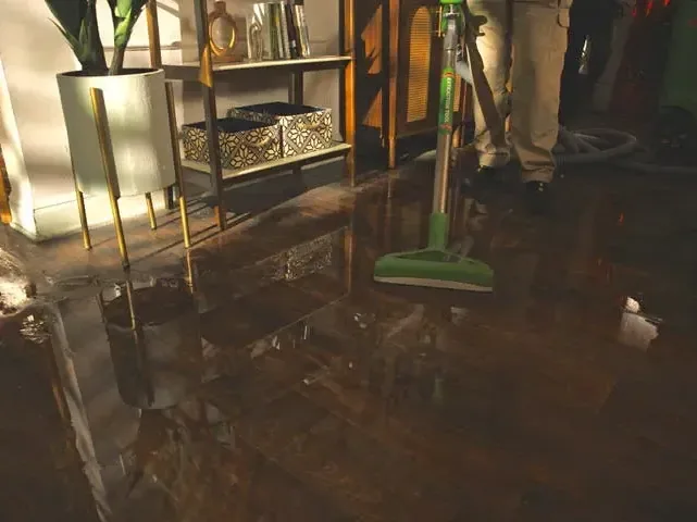 Standing floodwater reflects furniture and cleanup tools across the floor of a home
