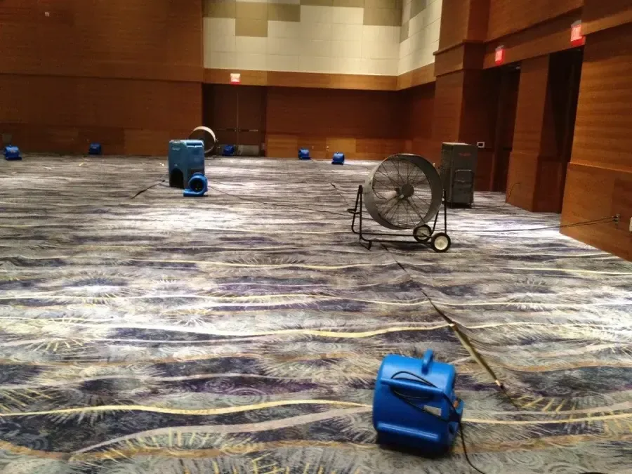 Air movers and dehumidification equipment dry carpet in a spacious event hall