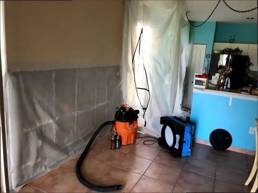 Drying equipment and protective sheeting stand beside opened walls in a water-damaged bathroom
