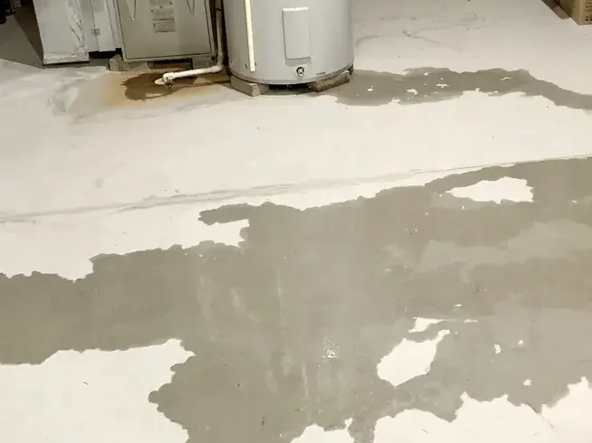 Water from a failed heater spreads over a garage floor beside the tank